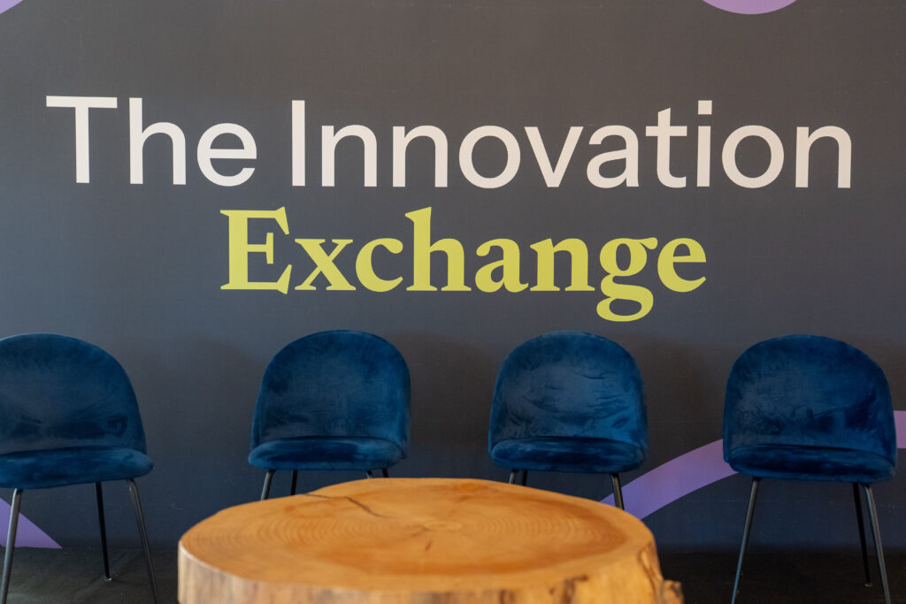 The Innovation Exchange backdrop with four blue chairs set for a panel.