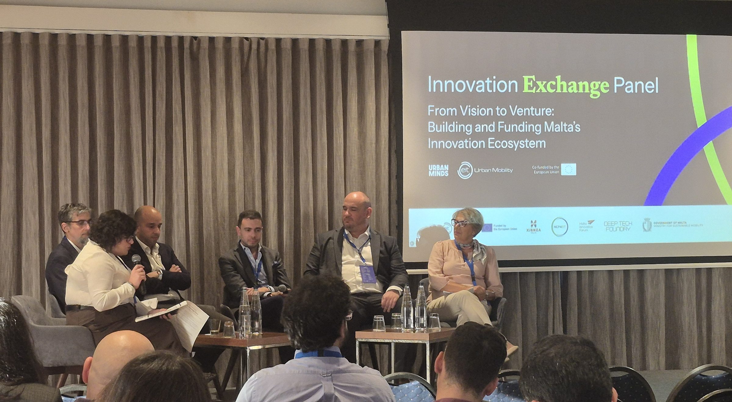 The moderator speaking to the five panellists, with the Innovation Exchange Panel title on screen.